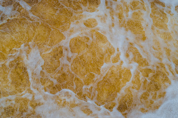 Water with foam. Yellow shade like gold or beer. Abstraction for background. Movement of colored water.