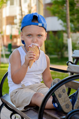 Boy in a blue cap and a white T-shirt is eating an ice cream cone
