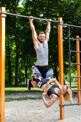 Young attractive couple doing pull-ups exercises on crossbar in a parrk at summer day