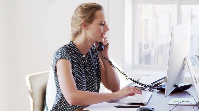 Young white woman using phone and computer in an office