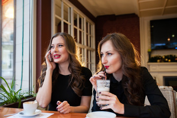 Two beautiful girls drinking coffee and talking on the phone