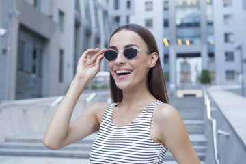 Portrait of beautiful smiling brunette woman in sunglasses on the background of an office building.