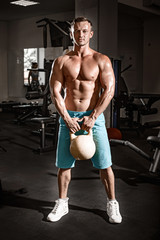 Fototapeta na wymiar Muscular bodybuilder guy doing exercises with weight in gym
