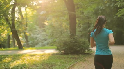 Back view of the young womanin the sport wear running in the park at the early morning.