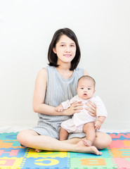 Portrait of happy asian mother hugging her cute little baby and looking in camera indoors