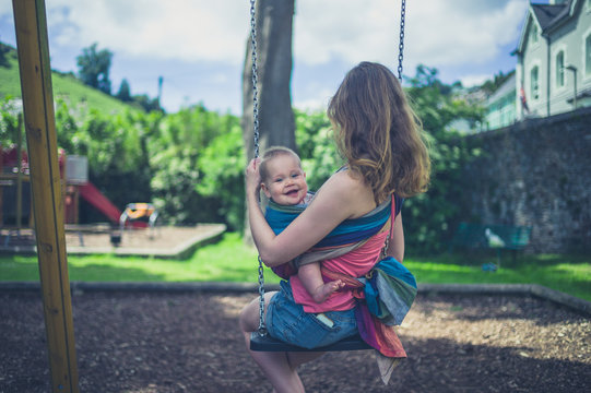 Young mother sitting on a swing with baby in sling