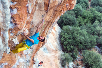 Mature Rock Climber ascending steep colorful rocky Wall Lead Climbing