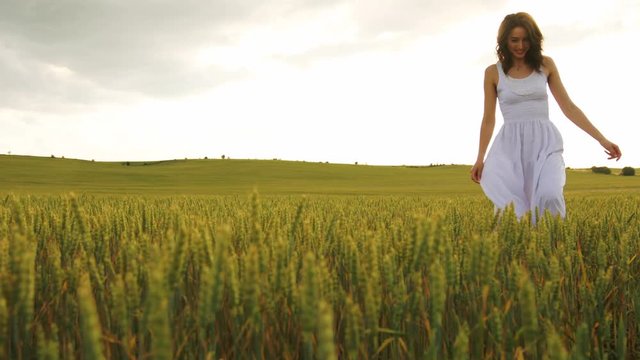 Emotional attractive woman in white dress playing with wheat spike in the field.