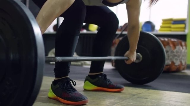 Tilt up with slow motion of muscular female weightlifter doing barbell snatch during workout