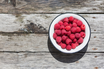 Raspberry in a white plate on an aged wood background. Top view.
