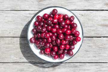 Cherry in a white bowl on a old wooden texture with rasty nails. Top view.