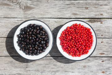 Red and black currant in a white bowl on a wooden texture with rusty nails. Top view. Copyspace.
