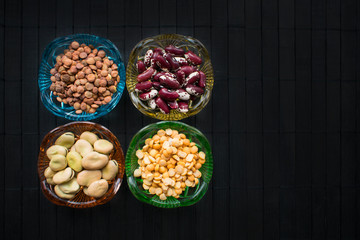 Different kind of beans and lentils in colored glass dishes on black wood background. Benefits for diet, weight control and diabetes. Health Benefits of Beans.