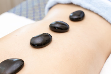 Beautiful Young Woman getting a hot stone on back at spa salon, health and healing concept.