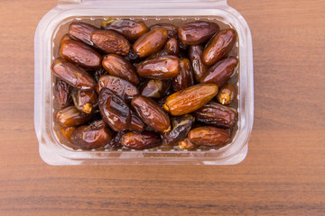 Dried date fruits in plastic container on wooden table. Top view