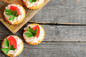 Home mini sandwiches with cream cheese on a wood background with empty place for text. Quick mini sandwiches from crackers cookies, spicy cream cheese, tomato and parsley. Tasty snack recipe. Top view