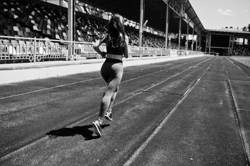 Portrait of a strong fit girl in sportswear running in the stadium. Black and white photo.