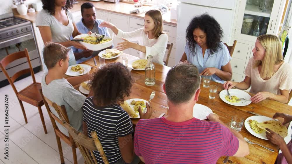 Wall mural two families with teenage children eating meal in kitchen