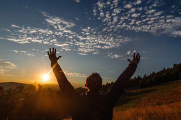 Human with hands up standing in mountains during a sunrise
