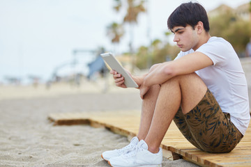 Young man sitting on beach holding tablet