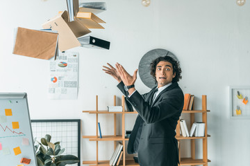 side view of young emotional businessman throwing folders with documents in office