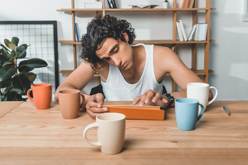 portrait of tired businessman in underwear using tablet while sitting at workplace with cups of coffee in office