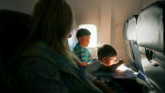 Flight on the aircraft. Children boys- kid baby and teen with mother , family in the seats of airplane interior. Child paints 