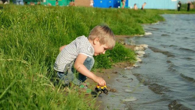 Joyful caucasian kid boy child baby plays a toy in water on the river bank. Nature, ecology and environment.