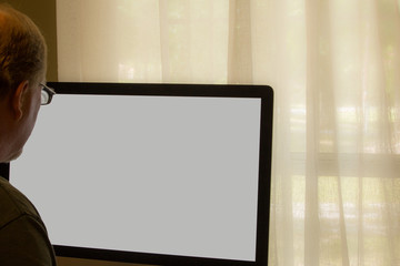 Man looking at blank computer screen near window 