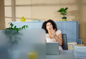 Woman yawning at desk in office