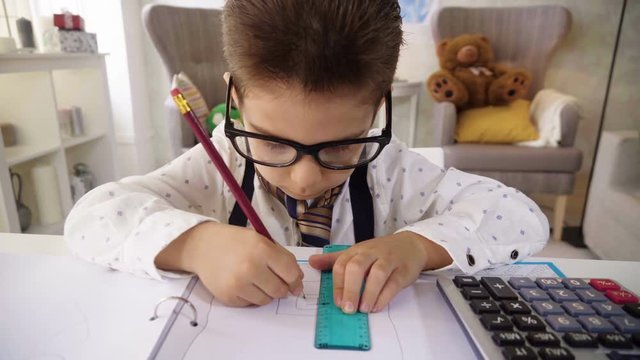 Small child boy in white shirt and tie images he is smart businessman working with papers and calculator, making notes, like adult professional, dreaming to be as his father, sitting at the table