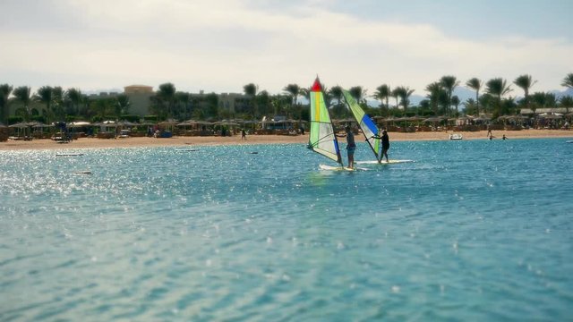 Holidaymakers people vacationers tourists train windsurfing at the Red Sea sunny seashore resort. Active rest and making healthy lifestyle, water sports in vacation holiday at summer. 