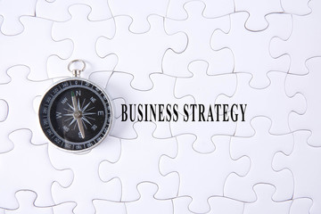 Jigsaw puzzle and compass with BUSINESS STRATEGY words.