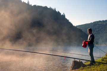 Naklejka premium Adult Man fishing early in the morning on mountain lake