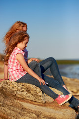 Little girl and her mother sitting on a rocky shore and looking at the sea.