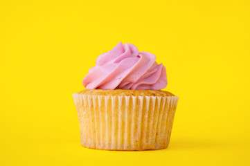 Cupcake with pink whipped cream on yellow background. The image with copy space. Background for the confectionery menu, cards, greetings, birthday invitations.