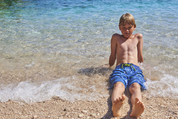 Young child boy having fun in the sea on the waves and enjoying water in summer holiday