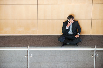 Businessman sitting in corridor using cellphone