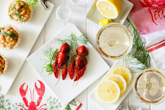 Two red boiled crayfish with twig of dill on the white plate, wooden rustic table . Two snaps glass of liquor with salt on edge, white vine. 