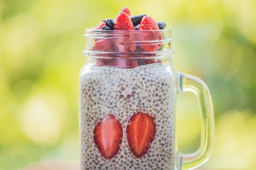 Healthy layered dessert with chia pudding, strawberry and honeysuckle in a mason jar on background...