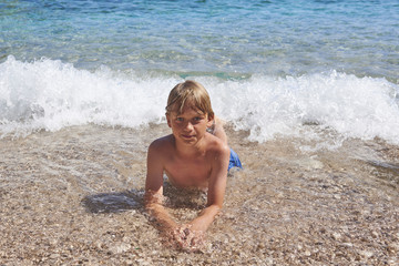 Young child boy having fun in the sea on the waves and enjoying water in summer holiday