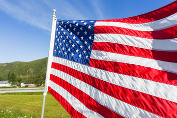 Flag of the United States of America (American flag or The Stars and Stripes, Old Glory, The Star-Spangled Banner) waving in the wind against summer forest landscape in sunny day.