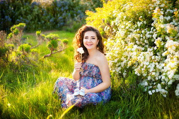 Happy pregnant woman, is wearing blue dress holding in hands bouquet of Dandelions flowers outdoors, new life concept