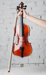 Holding violin with bow under white grand piano with brick wall background