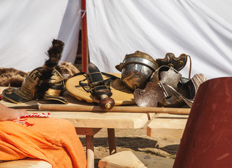 Fototapeta na wymiar Ancient warrior swords, shields and helmets on a wooden table in warm sunny day