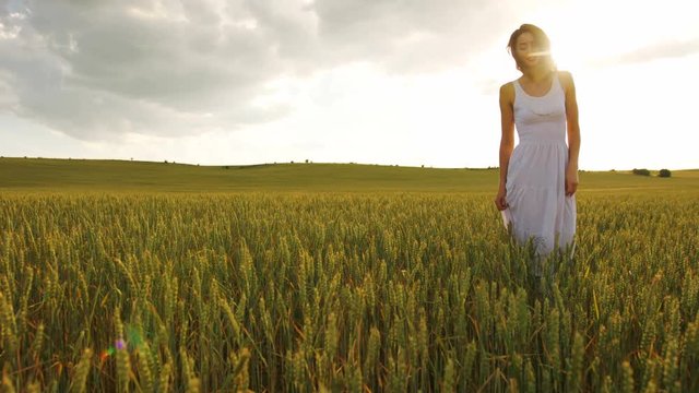 Young beatiful woman in white dress walking in the yellow field on the blue sky background.