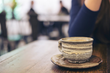 Closeup image of a woman sitting in cafe with ceramics cup of hot coffee on vintage wooden table in cafe