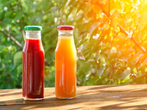 Two bottles of juice in the garden on a background of greenery, summer, sunlight