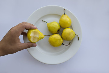 Bitten pear in hand near a white plate