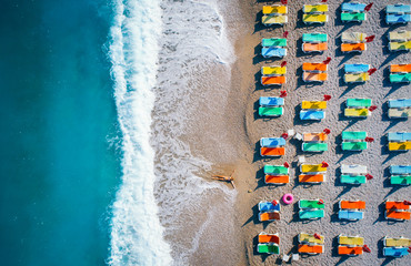 Beautiful young woman on the sea at sunrise in Oludeniz, Turkey. Aerial view of lying woman on the beach with colorful chaise-lounges. Top view from drone. Seascape with girl, azure water and waves © den-belitsky